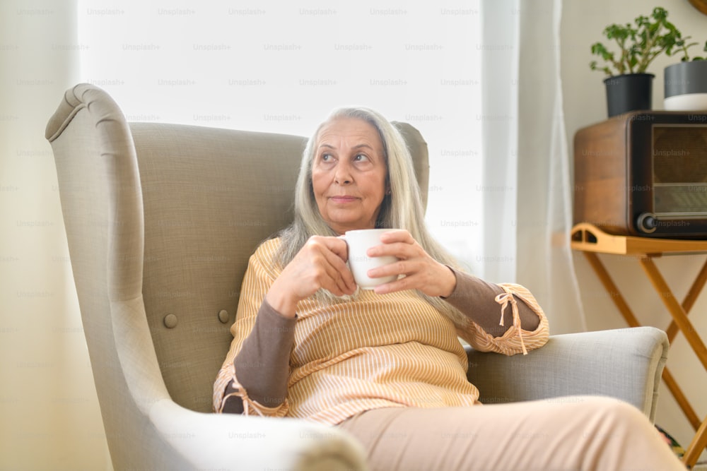 A relaxed senior woman with cup of tea sitting in armchair at home.