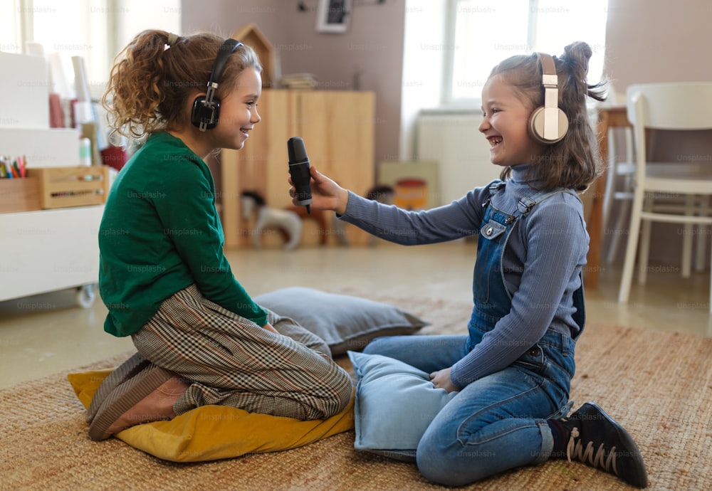 Happy little girls with headphones and microphone taking an interview, having fun and playing at home.