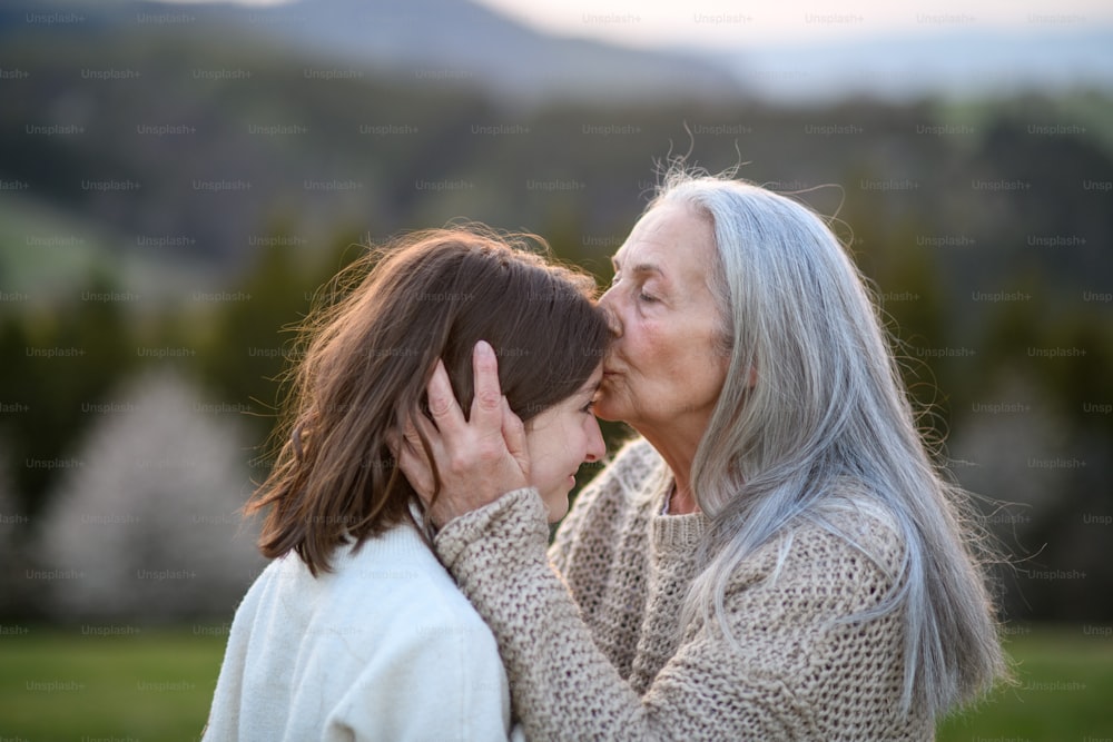 Une grand-mère âgée heureuse embrassant son grand-père adolescent sur le front dans la nature un jour de printemps.