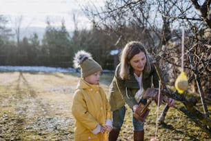 Un niño con síndrome de Down con su madre colgando una pajarera en el jardín en invierno juntos.