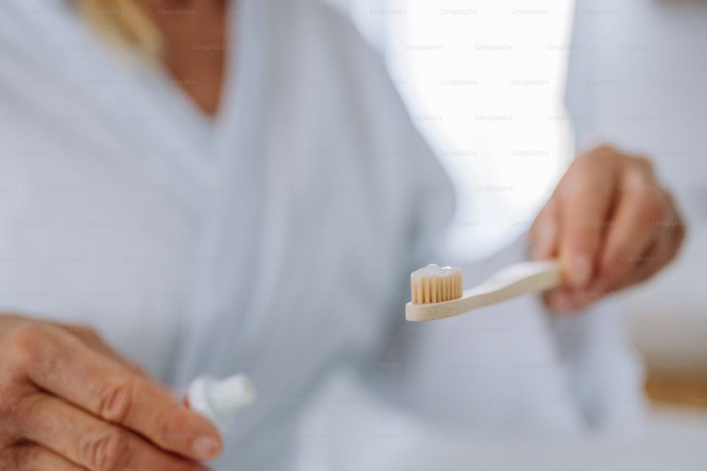 Un gros plan d’une femme tenant une brosse à dents en bois et un dentifrice naturel dans la salle de bain, mode de vie durable.