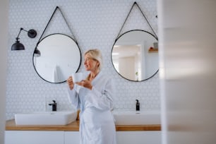 A beautiful senior woman in bathrobe drinking tea in bathroom, relax and wellness concept.