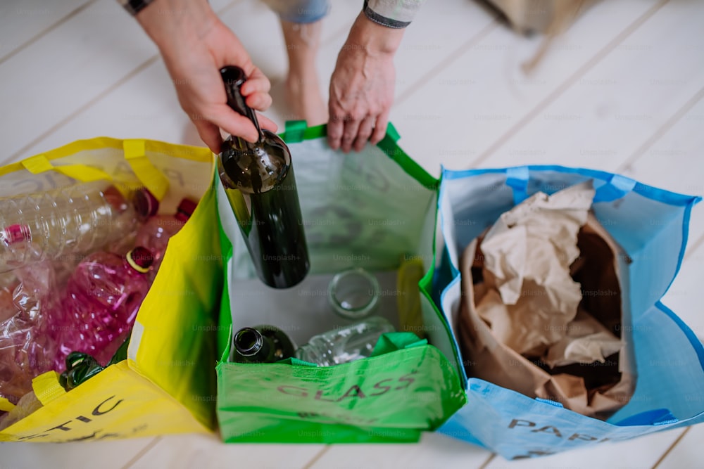 Sección media de una mujer tirando una botella de vidrio vacía en un contenedor de reciclaje en la cocina.