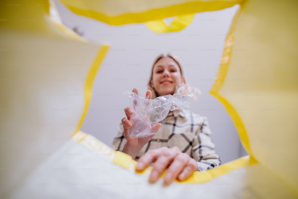Imagen desde el interior de una bolsa amarilla de reciclaje de una mujer tirando una botella de plástico para reciclar.