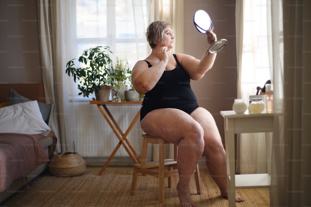 과체중 여성이 앉아서 집에서 거울을 보고 있다, 자기 관리 개념.