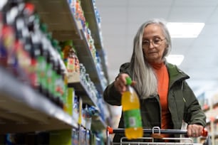 Anciana que compra y elige agua saborizada en el supermercado.