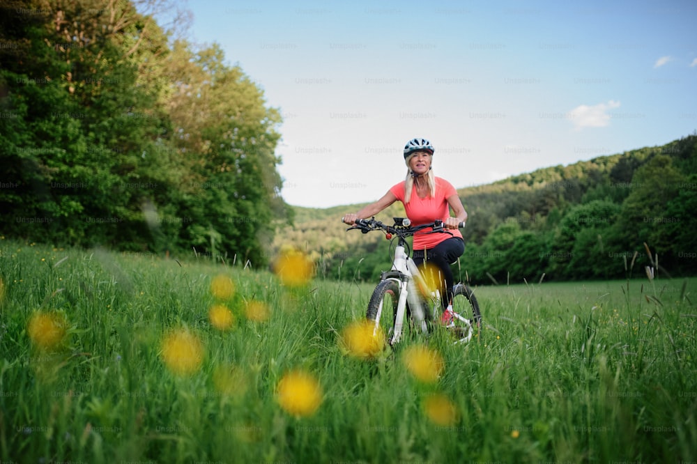 쾌활하고 활동적인 시니어 여성 바이커가 자연 속에서 야외에서 자전거를 타고 있습니다.