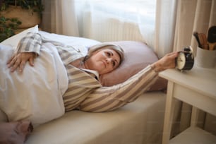 침대에서 일어나 집에서 알람 시계를 끄는 과체중 여성.