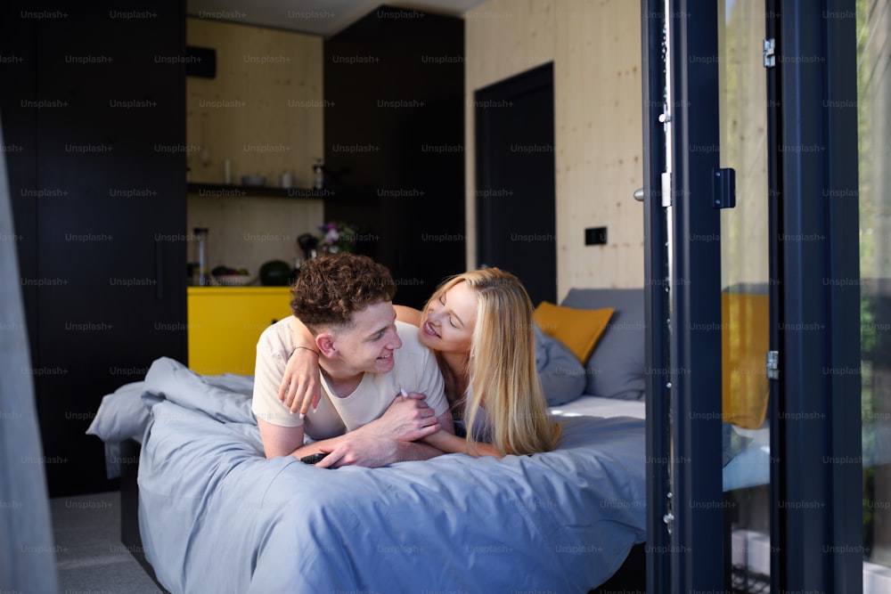 Ein junges, glückliches verliebtes Paar, das morgens im Bett liegt, in ihrem neuen Zuhause in einem winzigen Haus, nachhaltiges Wohnkonzept.