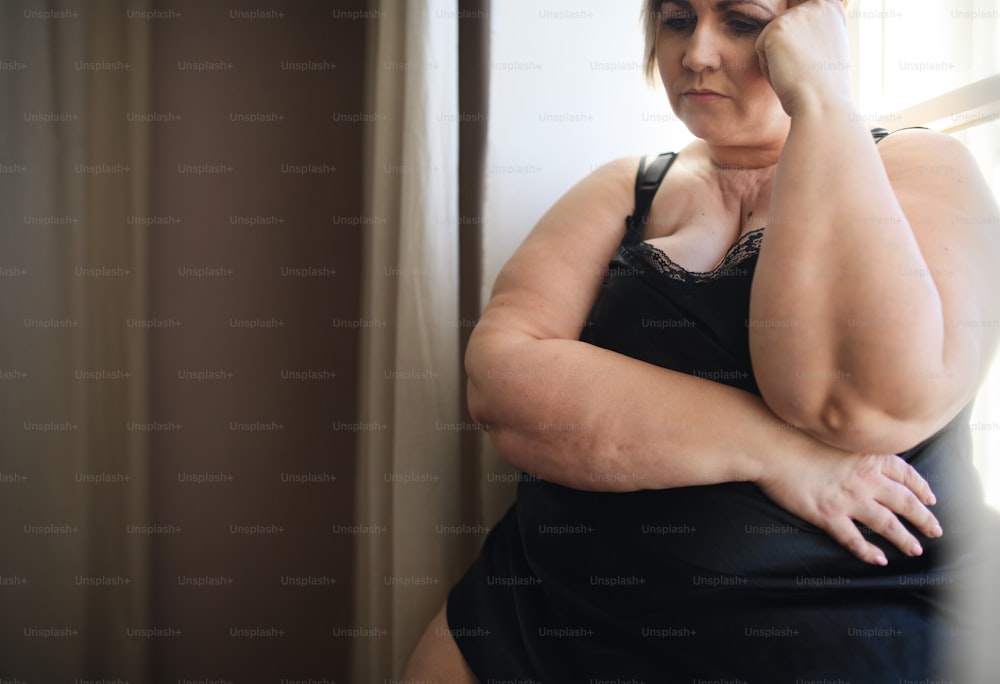 A depressed lonely fat woman in underwear looking down and thinking at home.