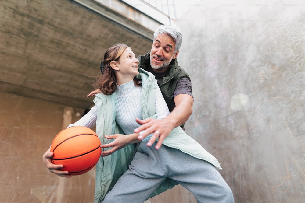 Um pai feliz e uma filha adolescente jogando basquete do lado de fora na quadra.