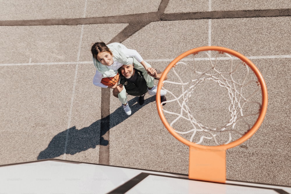 A father and teenage daughter playing basketball outside at court, high angle view above hoop net.