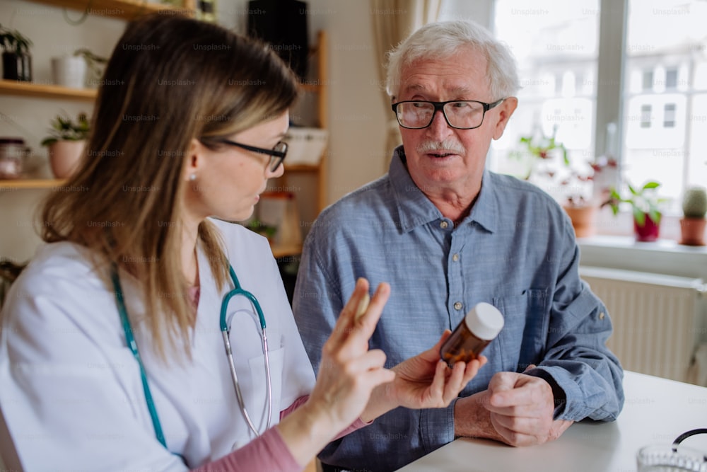 A healthcare worker or caregiver visiting senior man indoors at home, explaining medicine dosage.
