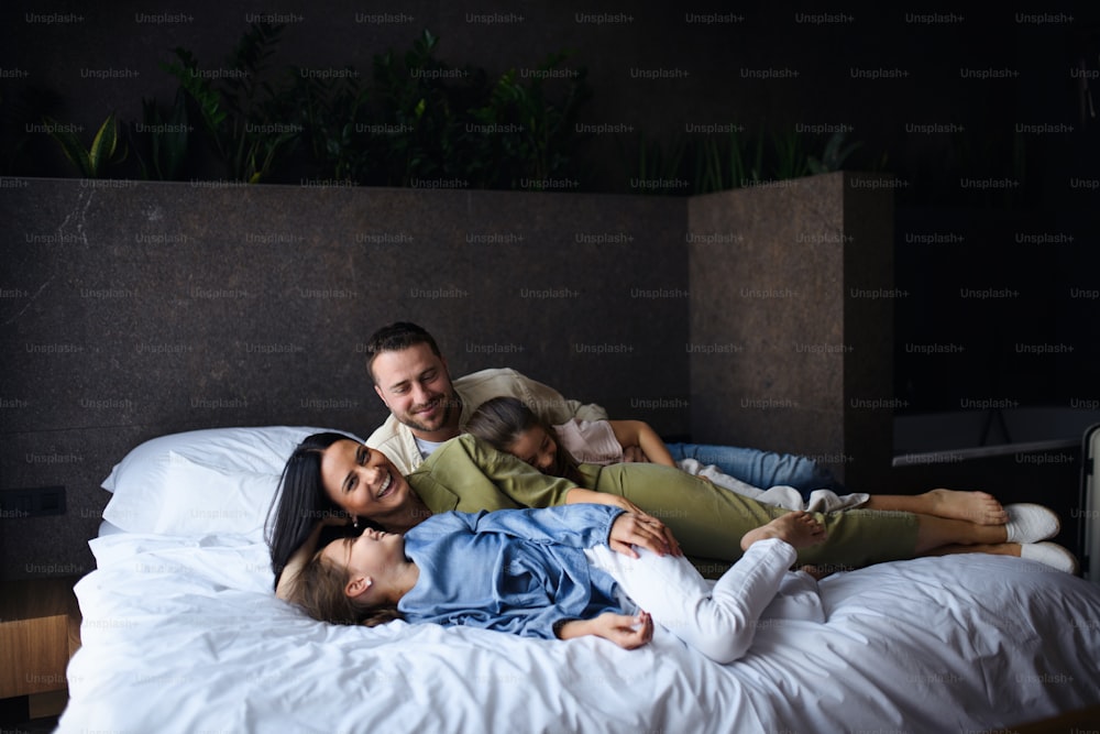 A happy young family with two children lying on bed at hotel, summer holiday.