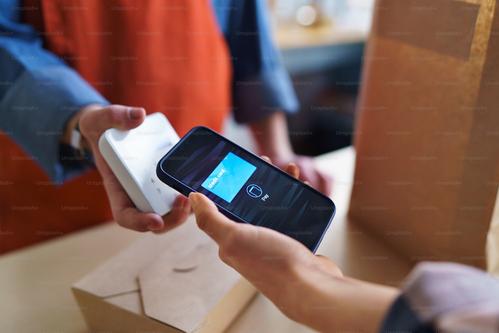 A close-up of waiter taking contactless smartphone payment from costumer in take away restaurant.