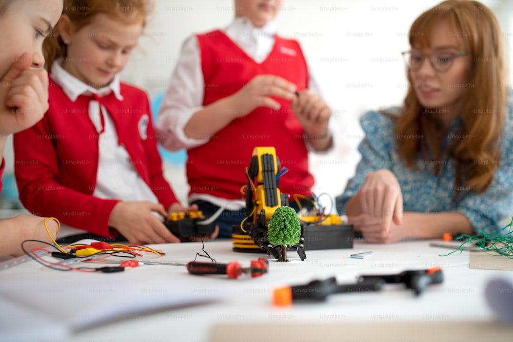 Un gruppo di bambini con un giovane insegnante di scienze che programmano giocattoli elettrici e robot in aula di robotica