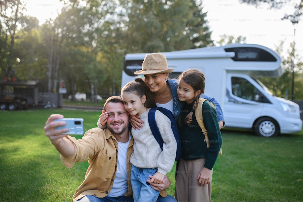 A happy young family with two children ltaking selfie with caravan at background outdoors.