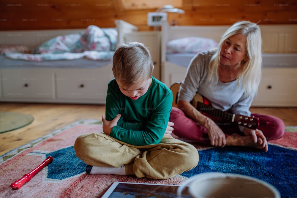 Ein Junge mit Down-Syndrom sitzt auf dem Boden und spielt mit seiner Großmutter zu Hause