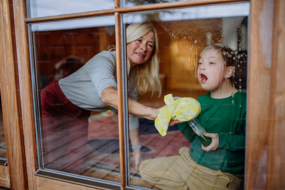 A boy with Down syndrome with his mother and grandmother cleaning window at home.