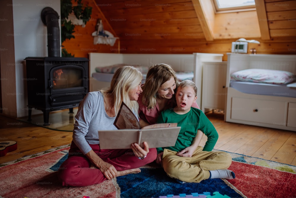 A boy with Down syndrome with his mother and grandmother looking at family photo album at home.