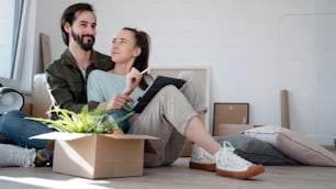 Ein junges Paar mit Tablet sitzt auf dem Boden und plant beim Einzug in eine neue Wohnung.