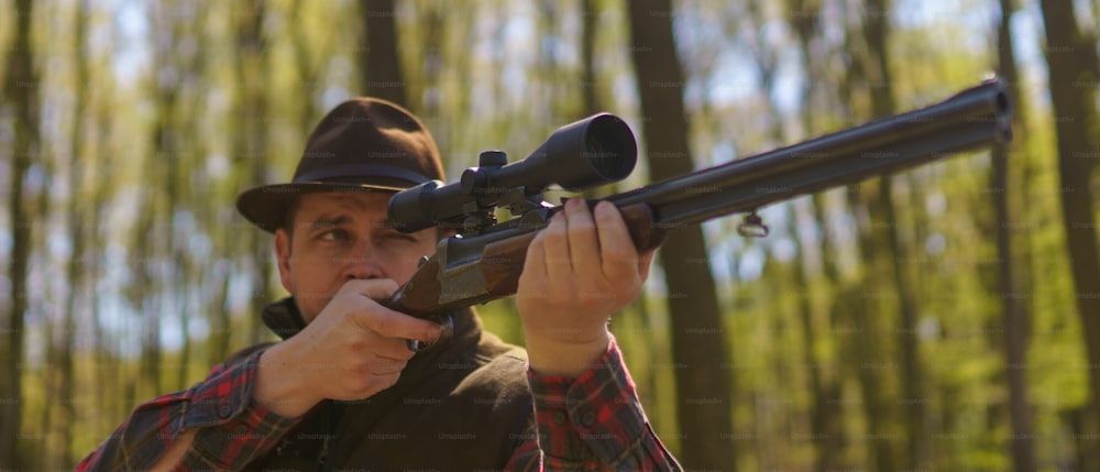 Un cazador apuntando con una pistola de rifle a una presa en el bosque.