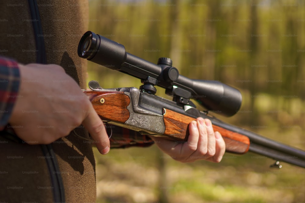 Um close-up de um homem caçador esperando com uma arma de fuzil em presas na floresta.