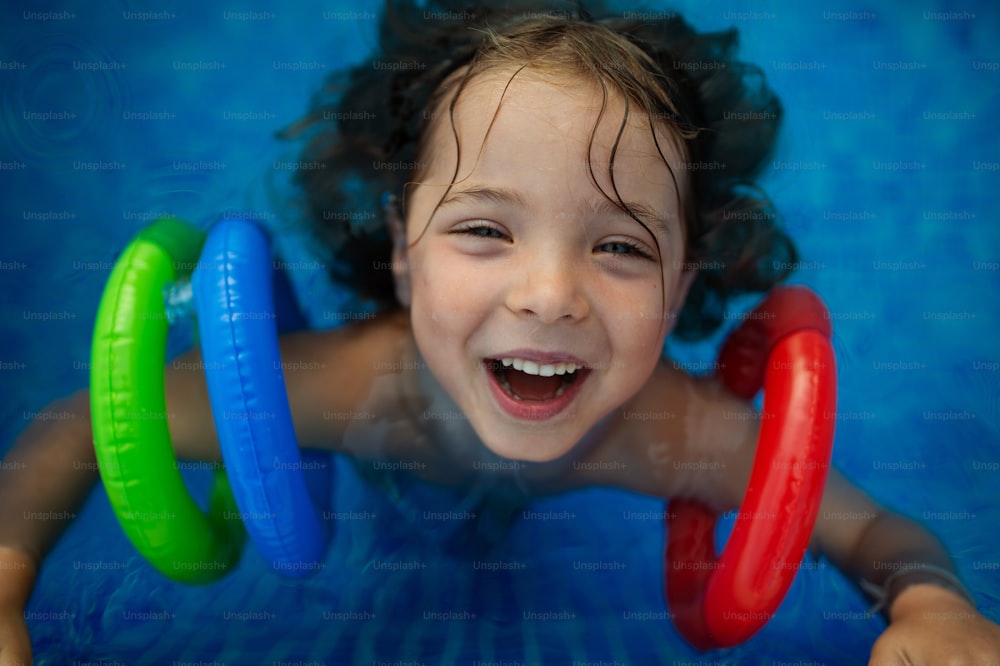 Una vista dall'alto di un bambino felice che indossa bracciali gonfiabili che giocano in piscina. Concetto di vacanza estiva.