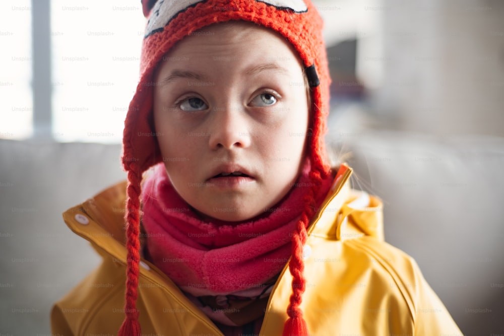 A little girl with Down syndrome looking at camera outoors in winter against brick wall.