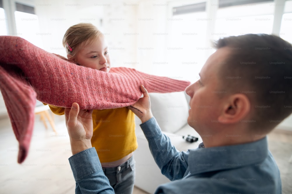 ダウン症の娘が家でジャンパーを着るのを手伝う父親。