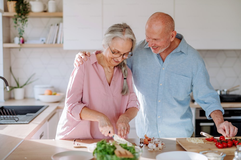 Um casal de idosos cozinhando e sorrindo juntos em casa.