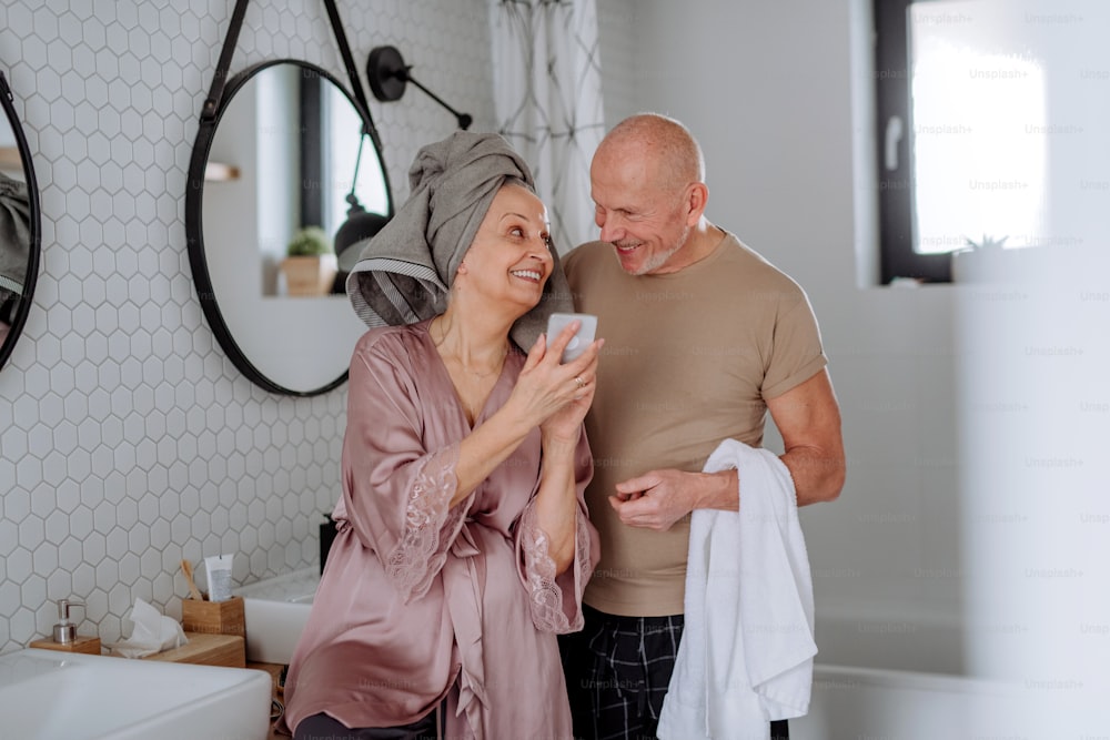 A senior couple in bathroom, useing telephone, talking and having fun, morning routine concept.