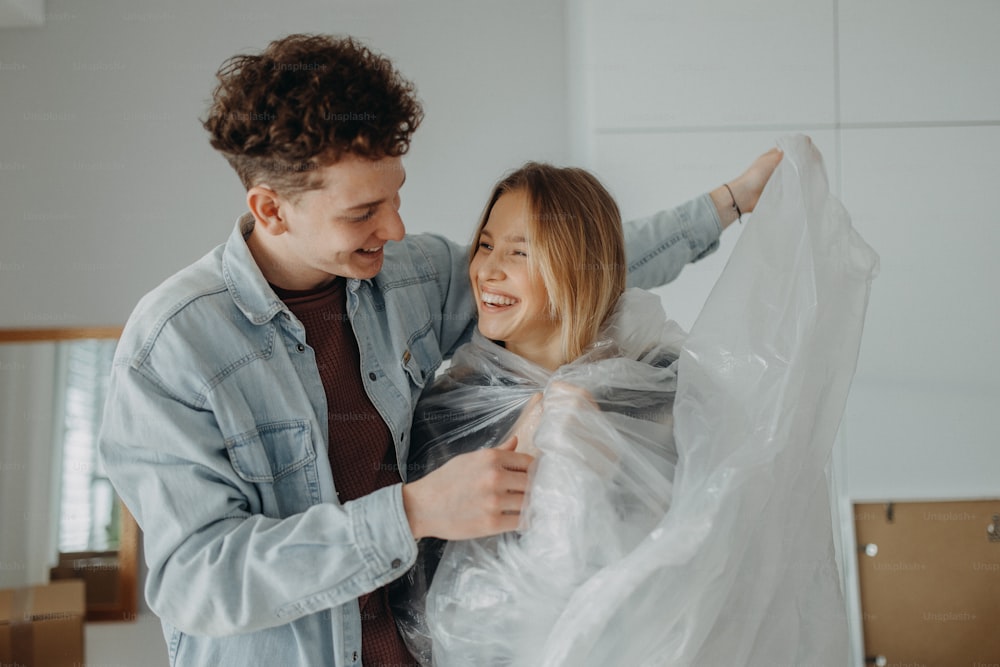 Una alegre pareja joven enamorada en su nuevo apartamento, divirtiéndose envolviendo papel de aluminio. Concepción de la mudanza.