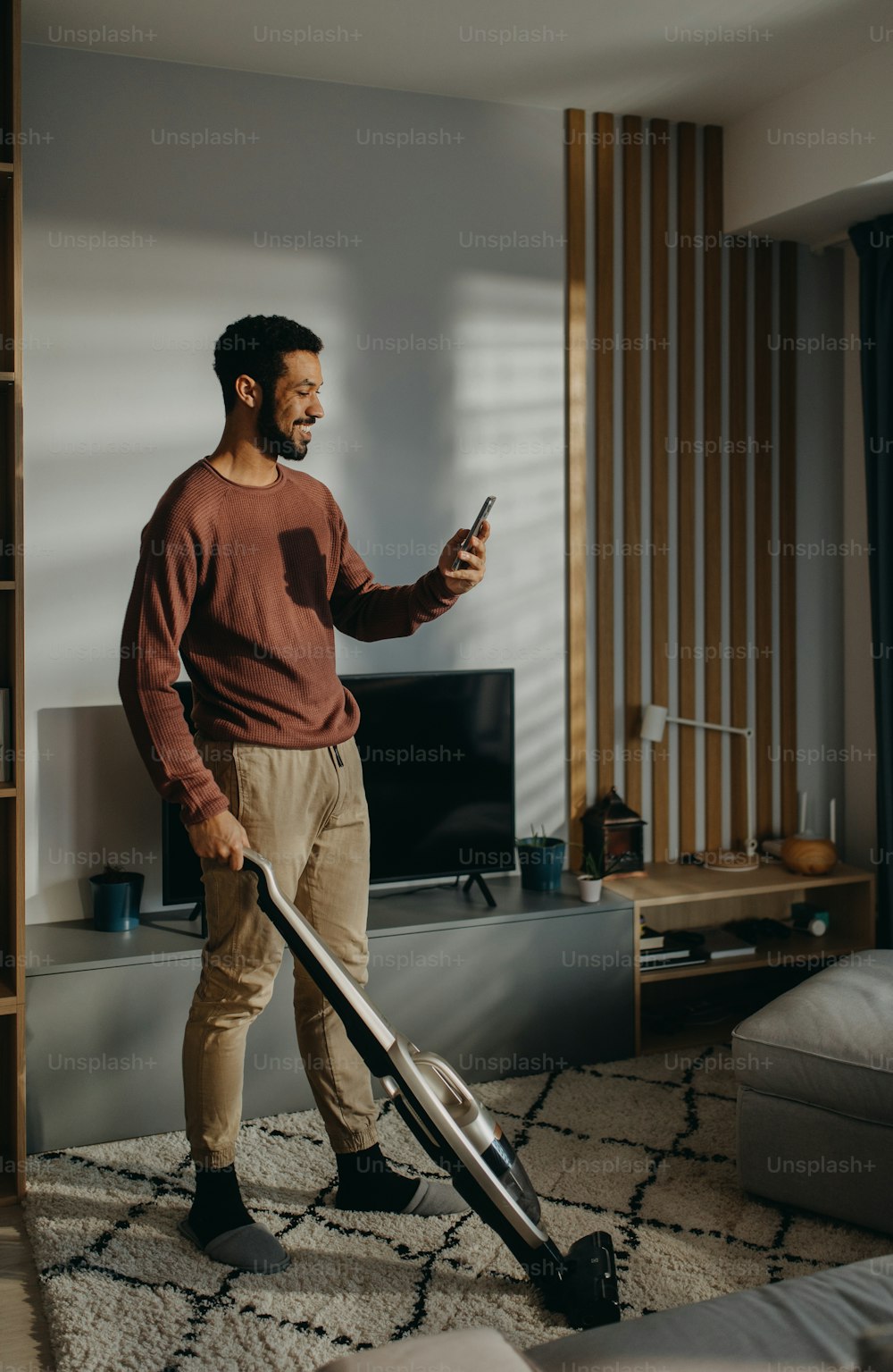 A young man vacuum cleaning carpet in living room