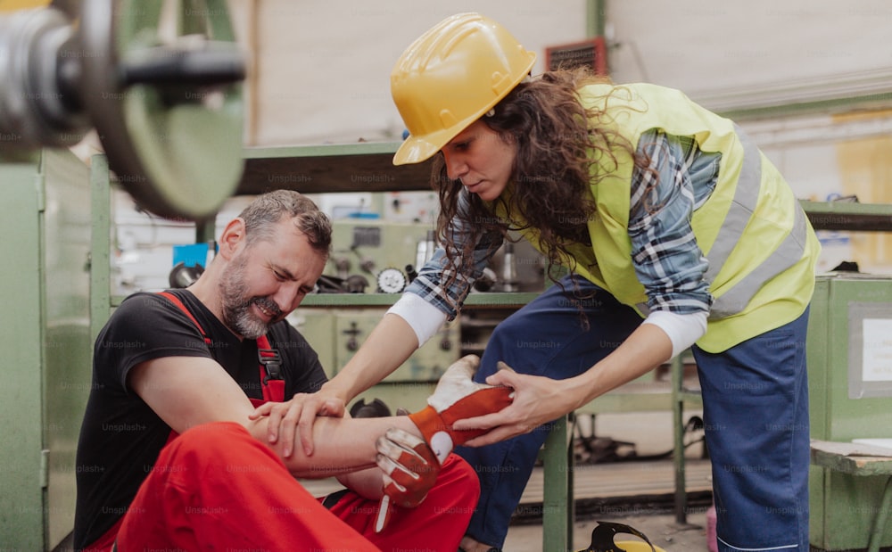 Una mujer ayuda a su colega tras un accidente en una fábrica. Apoyo de primeros auxilios en el concepto de lugar de trabajo.