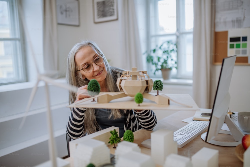 A senior woman architect holding model of modern eco buliding in office