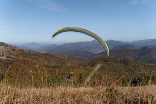 Un parapente volando en el cielo azul con la montaña de fondo.