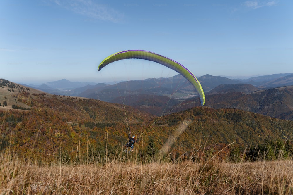 Un parapendio che vola nel cielo blu con la montagna sullo sfondo.