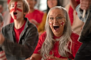 An excited senior woman football fan supproting English national team in live soccer match at stadium.