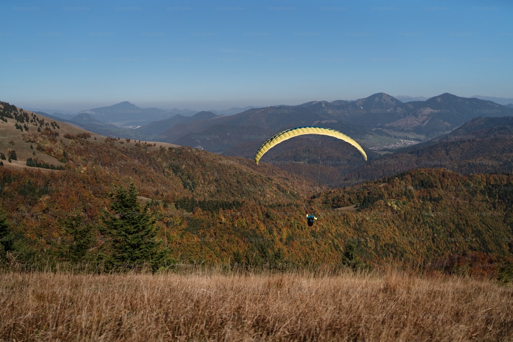 Um parapente voando no céu azul com a montanha ao fundo.