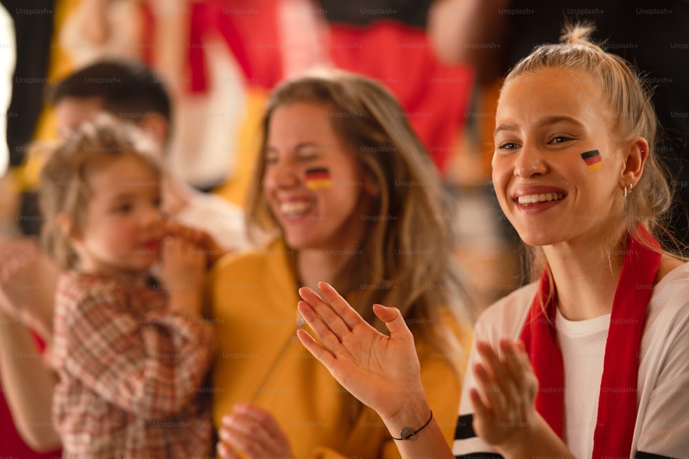 Excited football fans, supproting a German national team in live soccer match at stadium.