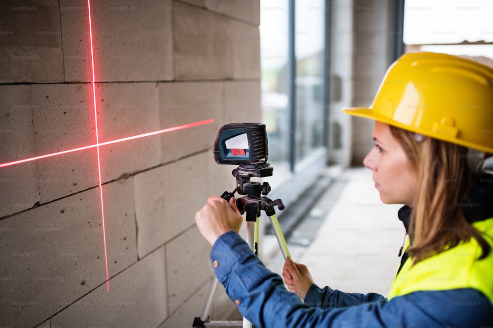 Female worker on the building site. Beautiful young woman with line laser level. House construction.
