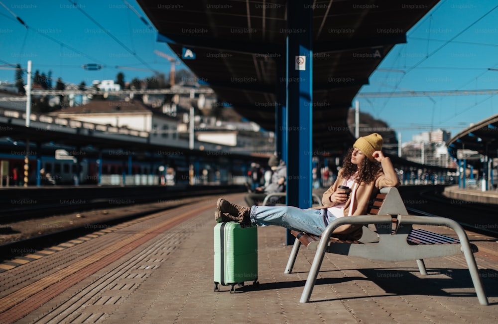 Eine junge Reisende sitzt allein am Bahnsteig mit Gepäck.