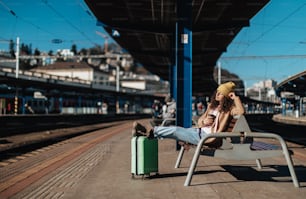 A young traveler woman sitting alone at train station platform with luggage.