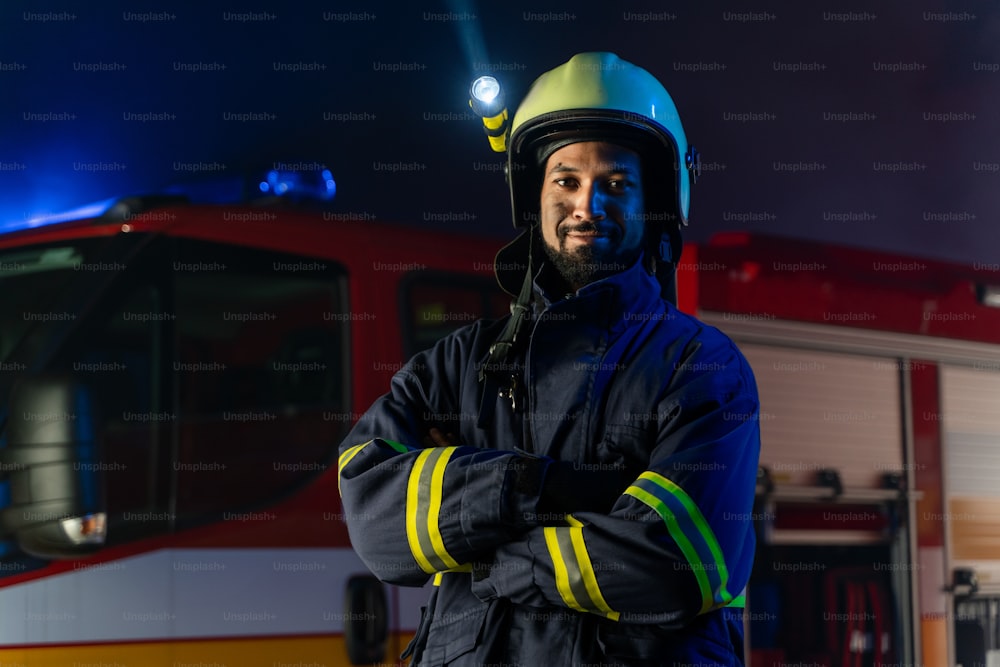 Ein Porträt eines schmutzigen Feuerwehrmannes im Dienst mit Feuerwehrauto im Hintergrund in der Nacht, lächelnd.