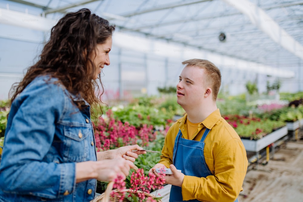 Um jovem funcionário feliz com síndrome de Down trabalhando no centro de jardinagem, recebendo pagamento do cliente.