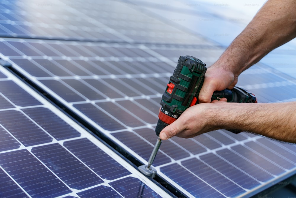 A man worker installing solar photovoltaic panels on roof, alternative energy concept. Close up hands with drill.
