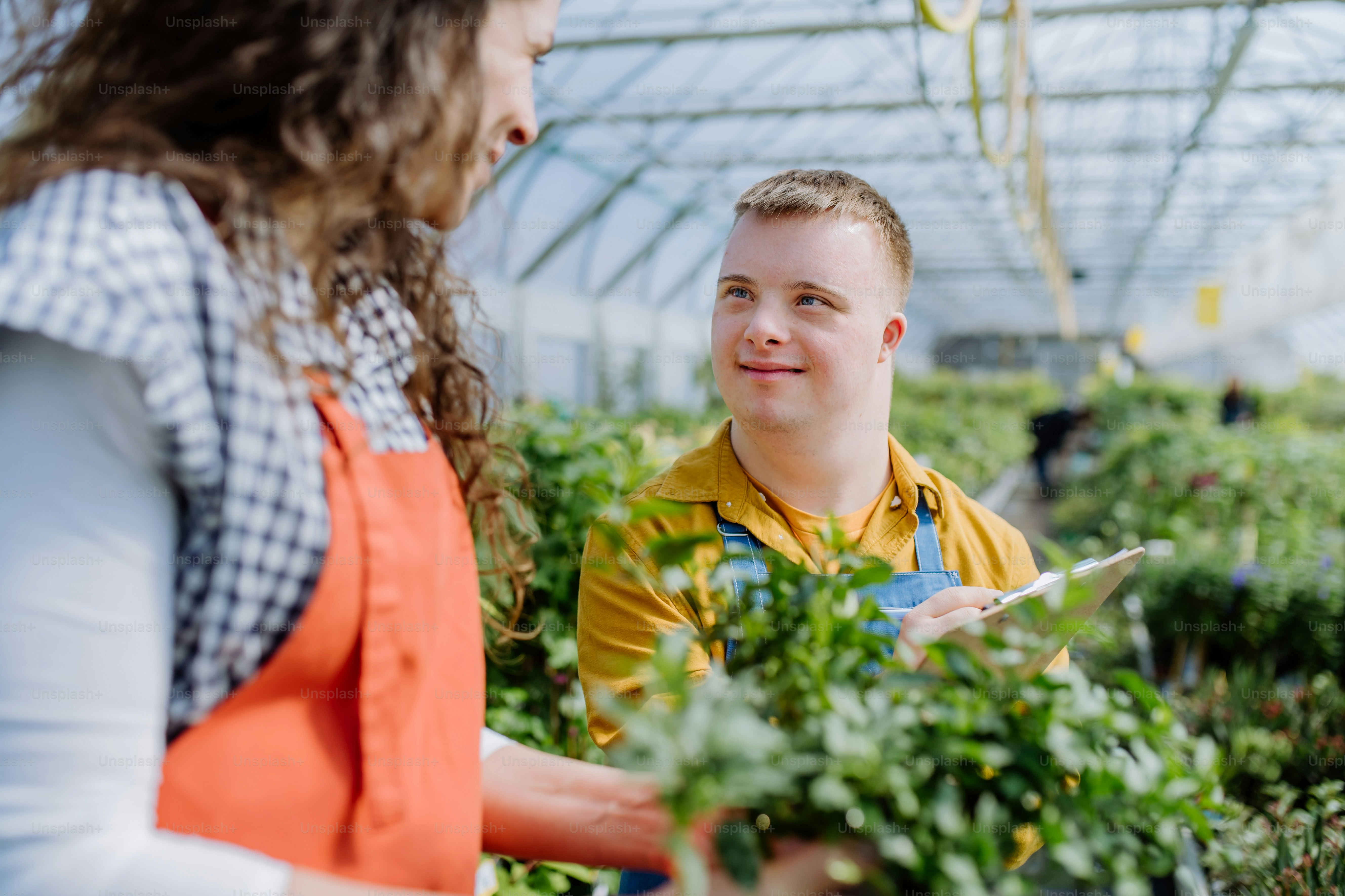 An experienced woman florist helping young employee with Down syndrome in garden centre