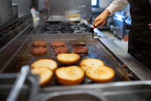 A close-up of professional female chef preparing burgers indoors in restaurant kitchen.