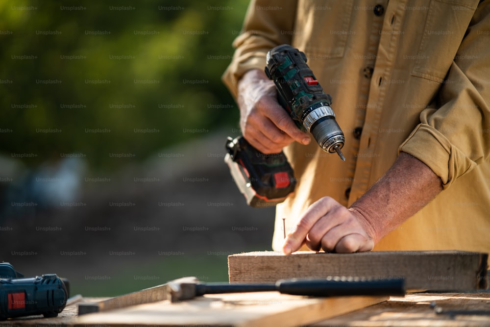 A close-up of handyman carpenter working in carpentry diy workshop outdoors with drill.
